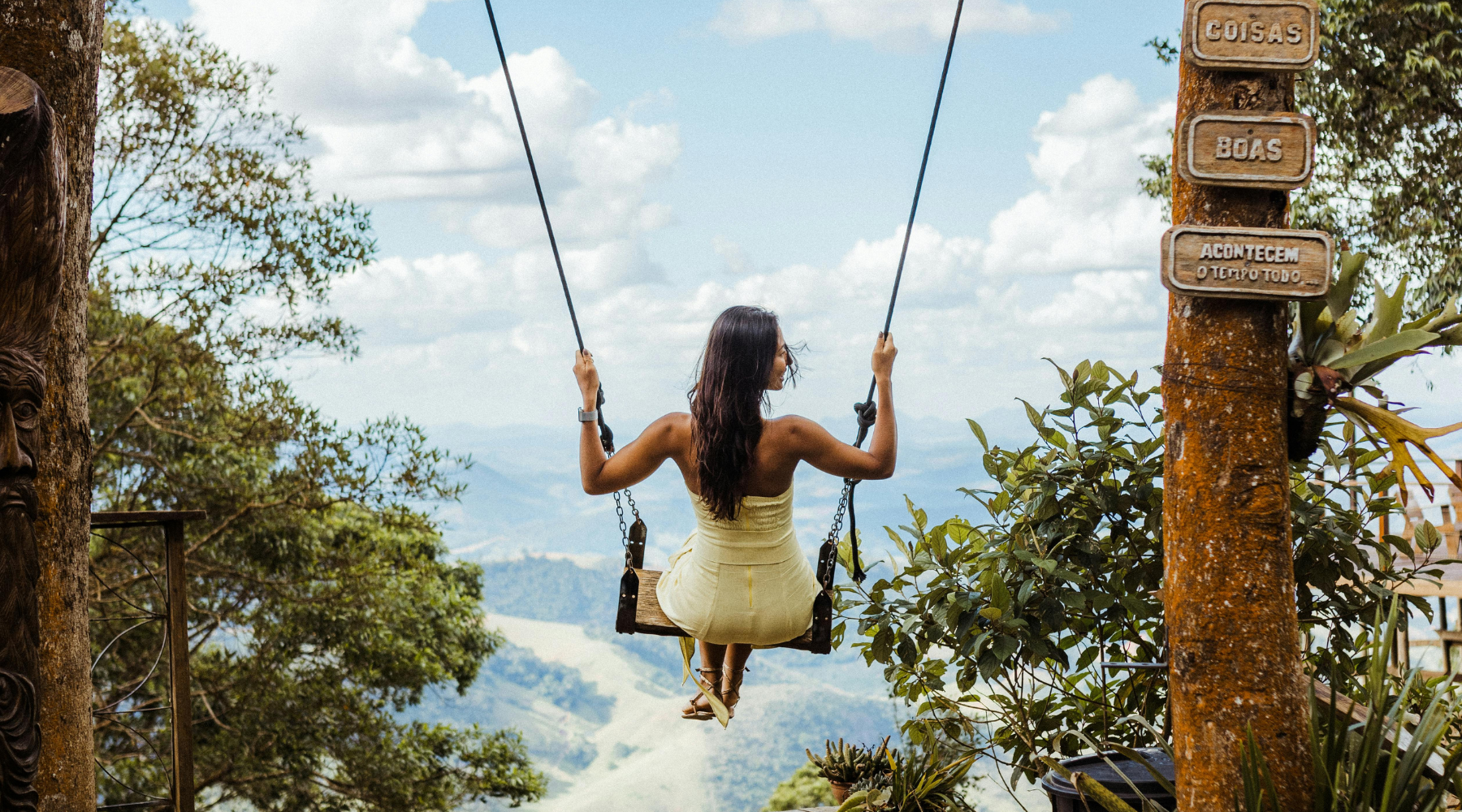 A woman on a swing overlooking a vast mountain valley, representing the global expansion and 'Going Global' vision of Crunchy Mama Box and Wellness Real Estate