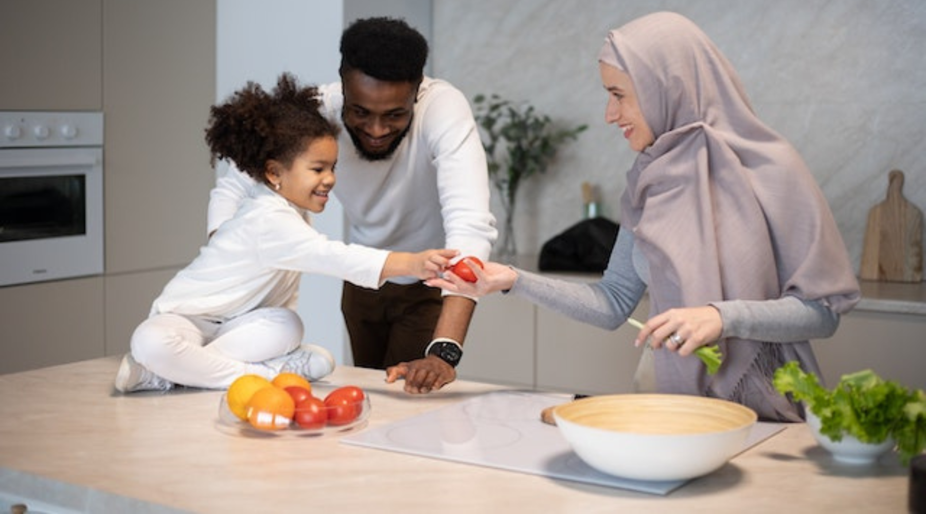 Young girl sitting on kitchen counter handing over a tomato to her mom